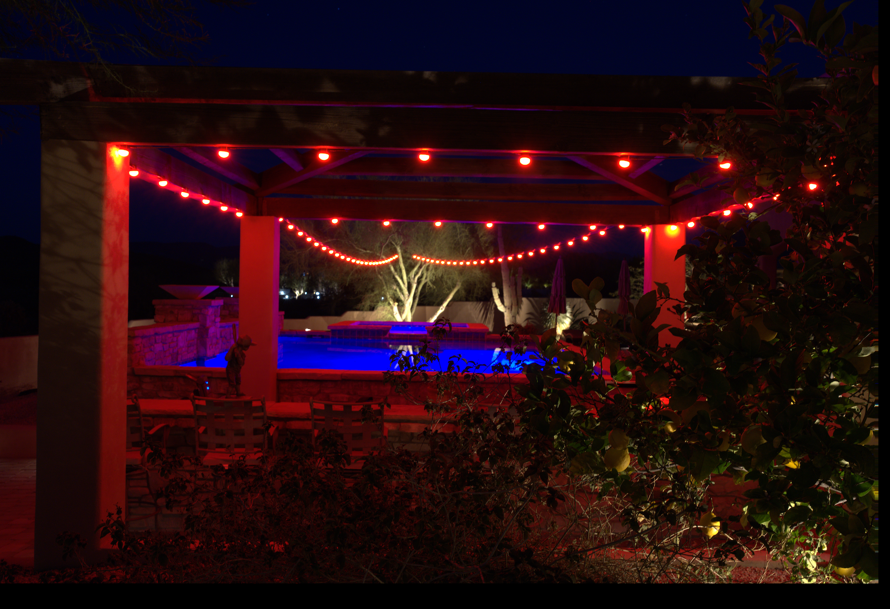 Pavilion with string lights at night, overlooking a pool area.
