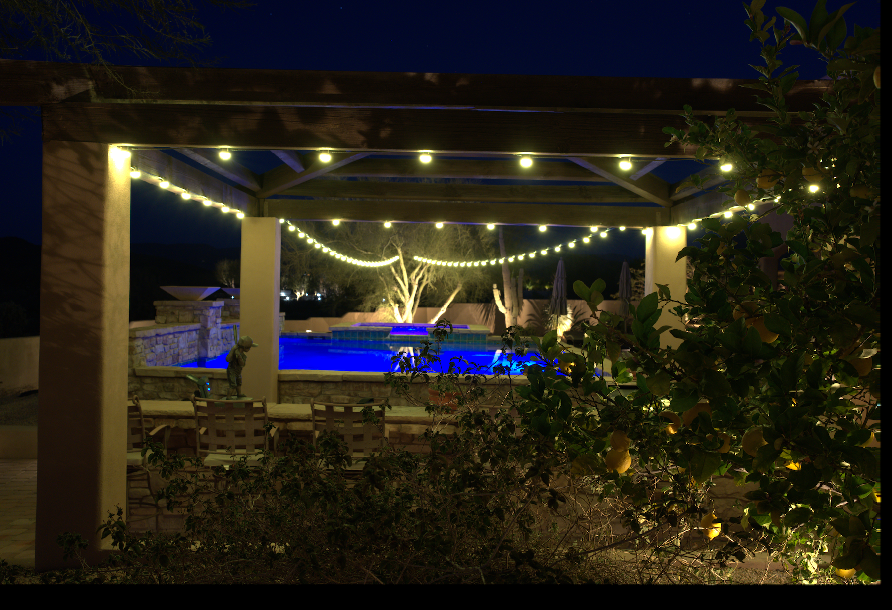 Outdoor pool area with string lights and a pergola at night.